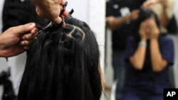 Valery Díaz se cubre la cara mientras se corta el cabello a cambio de dinero en un salón de belleza en Caracas, Venezuela, el viernes 5 de abril de 2019. (AP Foto / Natacha Pisarenko)