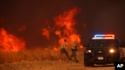 Policías del condado vuelven a su vehículo tras observar las llamas provocadas por el incendio Hughes junto a una carretera en Castaic, California, el 22 de enero de 2025.