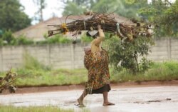 FILE - A woman with a baby strapped on her back carries firewood for cooking on the streets of Harare, Zimbabwe, March 2, 2021.