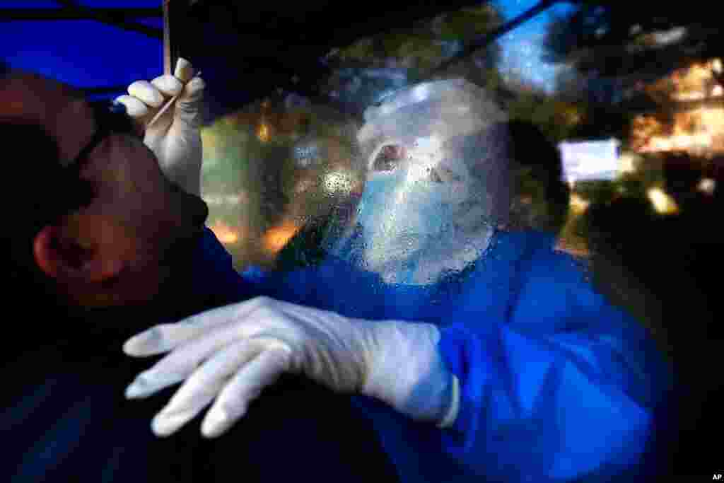 Separated by a plastic barrier, Nurse Mariel Portillo takes a swab sample from a man for a COVID-19 test outside the General Hospital in Luque, Paraguay.