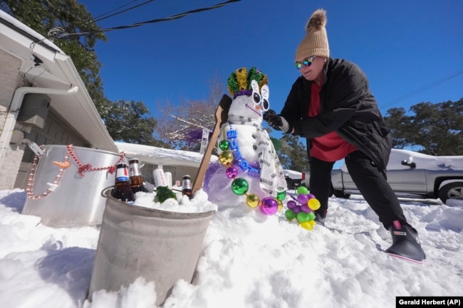 Stacy Centanni refreshes her Mardi Gras festooned snowman as it melts, the day after a record-setting snowstorm in River Ridge, La., a suburb of New Orleans, Wednesday, Jan. 22, 2025.