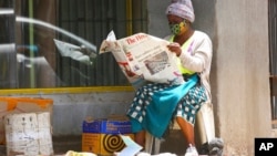 FILE - A masked vendor reads a newspaper in Harare, Jan,5, 2021. At the time, Zimbabwe began a 30-day lockdown to rein in a spike in COVID-19 infections. On Feb. 12, 2021, the government said a free COVID-19 vaccination program would begin "immediately."