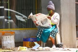 FILE - A masked vendor reads a newspaper in Harare, Jan,5, 2021. At the time, Zimbabwe began a 30-day lockdown to rein in a spike in COVID-19 infections. On Feb. 12, 2021, the government said a free COVID-19 vaccination program would begin "immediately."