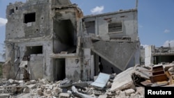 FILE - Saher al-Ali's family members stand inside their damaged house in the rebel-held town of Nairab, Idlib region, Syria, April 17, 2020. 