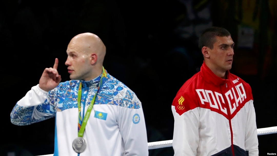Petinju peraih medali perak Vassiliy Levit dari Kazakhstan (kiri) meminta penonton diam sementara peraih medali emas Evgeny Tishchenko dari Rusia berdiri di sebelahnya saat lagu kebangsaan dikumandangkan di Olimpiade Rio de Janeiro (15/8). (Reuters/Yves Herman)