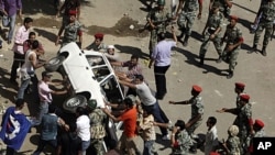 Protesters and military police tussle over trying to overturn a police car after protesters broke the windows in front of the court complex in Suez, Egypt, July 6, 2011