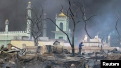 A man stands in front of a mosque as it burns in Meikhtila, Burma, Mar. 21, 2013.