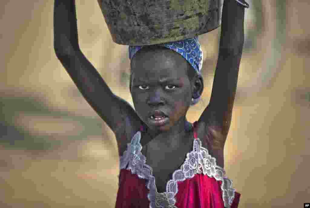 A young displaced girl carries a bucket of water back to her makeshift shelter at a United Nations compound which has become home to thousands of people displaced by the recent fighting, in the Jebel area on the outskirts of Juba.
