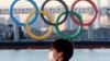 Seorang pria mengenakan masker di tengah pandemi COVID-19, dengan latar belakang Cincin Olimpiade raksasa di Tokyo, Jepang, 13 Januari 2021. (REUTERS/Kim Kyung-Hoon//File Photo)