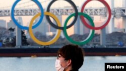 Seorang pria mengenakan masker di tengah pandemi COVID-19, dengan latar belakang Cincin Olimpiade raksasa di Tokyo, Jepang, 13 Januari 2021. (REUTERS/Kim Kyung-Hoon//File Photo)