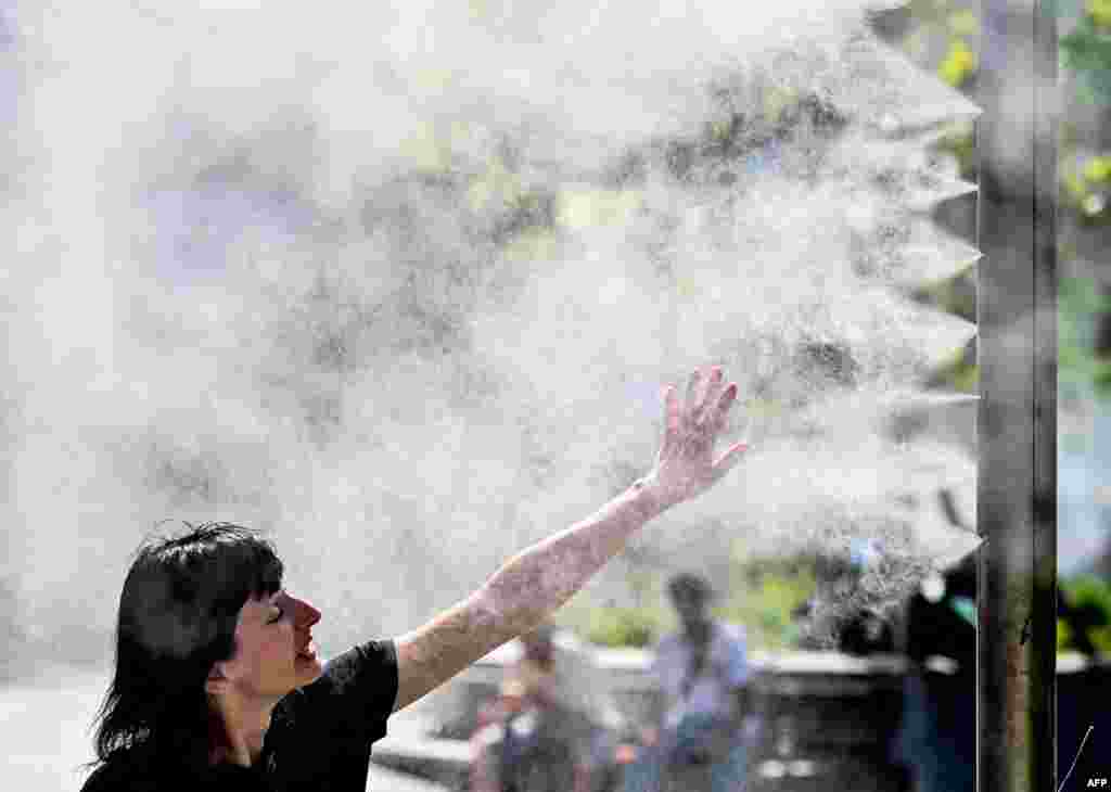 A woman cools down by a water sprayer in Vienna, Austria on a warm day.