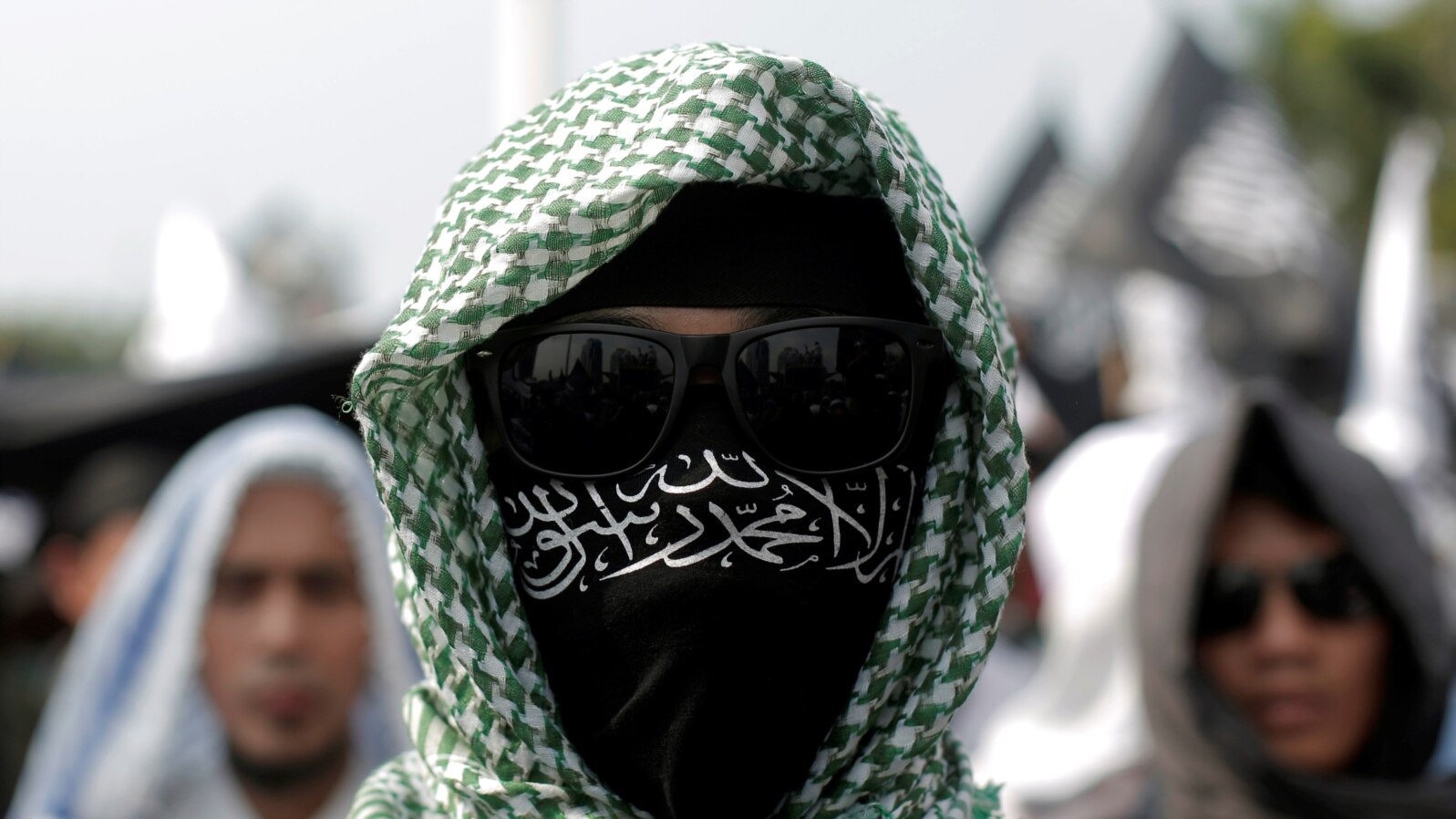 FILE - An Islamic group member covers his face with Hizbut Tahrir flag during a protest against the decree allowing the government to disband organizations deemed to run counter to the secular state, in Jakarta, July 28, 2017.