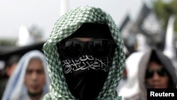 FILE - An Islamic group member covers his face with Hizbut Tahrir flag during a protest against the decree allowing the government to disband organizations deemed to run counter to the secular state, in Jakarta, July 28, 2017.