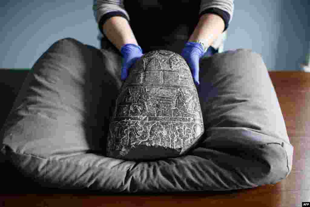 A gallery assistant poses with a Babylonian cuneiform kudurru (boundary stone) which was looted from Iraq at the British museum in London. The kudurru, seized at London&#39;s Heathrow airport in 2012, was handed over to representatives of the Iraq embassy at the British museum.