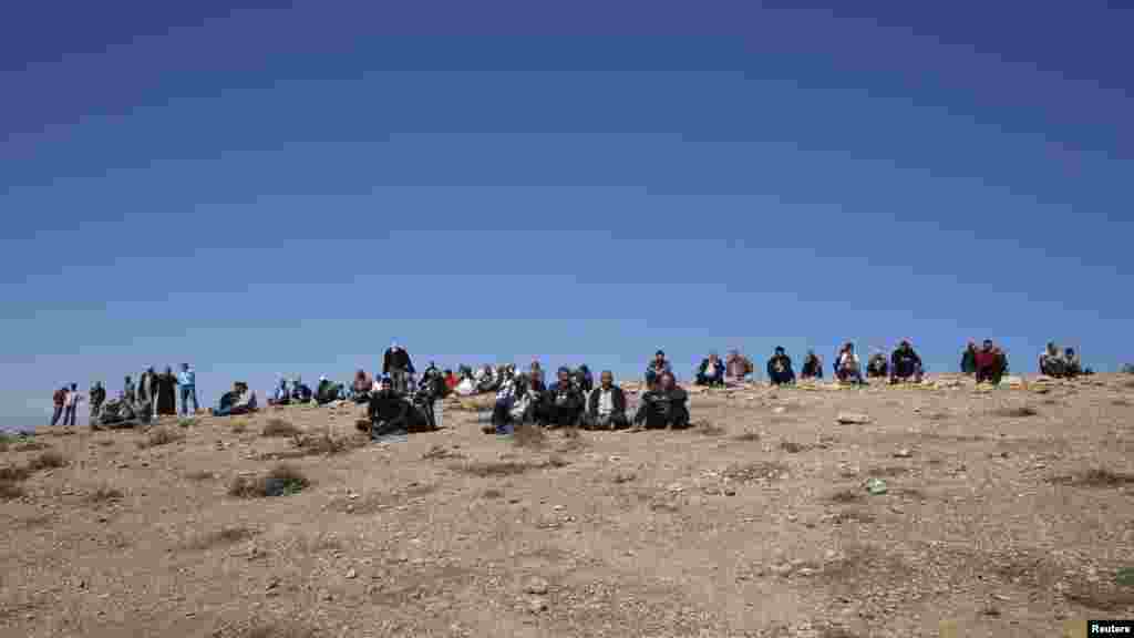 People sit on a hilltop on the outskirts of Suruc, at the Turkey-Syria border, overlooking Kobani, Syria, as they watch from the distance, fighting between Syrian Kurds and the militants of the Islamic State group, Oct. 18, 2014. 