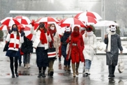 Women wearing carnival masks march down the streets under umbrellas with the colors of the former white-red-white flag of Belarus to protest against the Belarus presidential election results in Minsk, on Jan. 26, 2021.