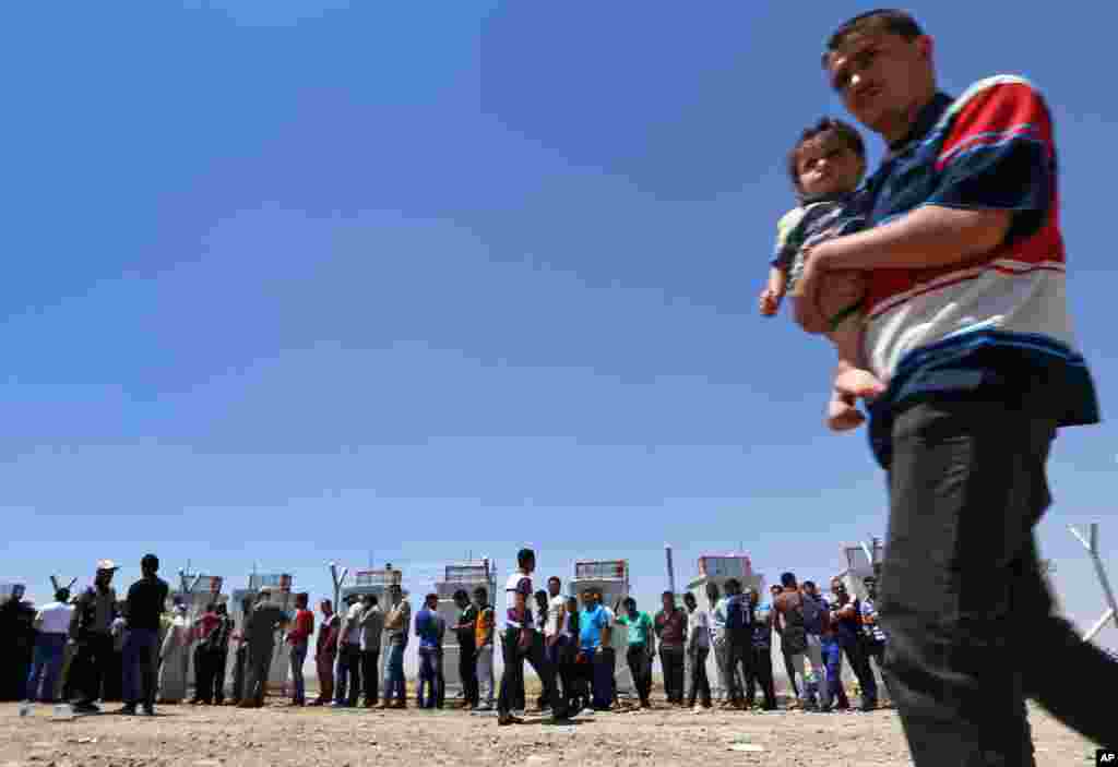 Iraqis who have fled the violence in their hometown of Mosul line up at Khazir refugee camp outside of Irbil, June 16, 2014. 