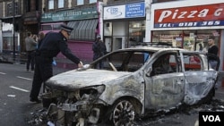 Seorang polisi memeriksa sebuah mobil dinas kepolisian yang hangus terbakar akibat kerusuhan di Tottenham, Minggu (7/8).