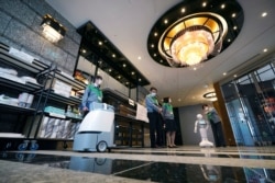 Tokyo Gov. Yuriko Koike, right, observes a cleaning robot operated at the lobby of a hotel for the new coronavirus COVID-19 patients with mild symptoms during a media preview in Tokyo, May 1, 2020.