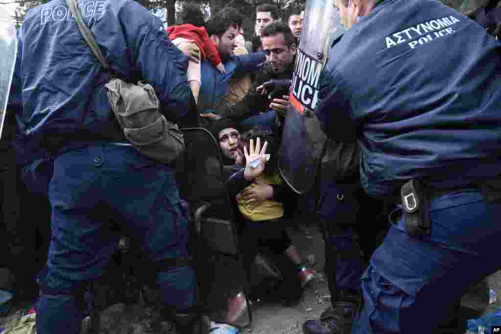 A woman tries to protect her daughter as refugees scuffle with the Greek police in their effort to reach the borderline with Macedonia, near the Greek village of Idomeni.