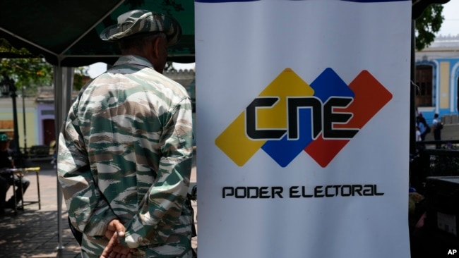 Un miembro de la milicia venezolana hace guardia al lado de un afiche del Consejo Nacional Electoral en Caracas, el 16 de abril de 2024.