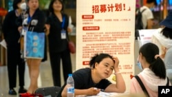 FILE - A recruiter talks with an applicant at a booth at a job fair at a shopping center in Beijing, on June 9, 2023.