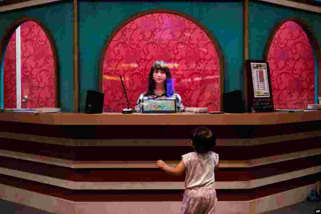 A baby girl looks at a humanoid robot sitting in a box office in Tokyo.