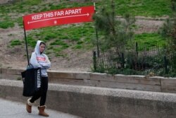 A woman passes a sign demonstrating the amount of space people should allow between each other to avoid contracting or spreading coronavirus as she leaves Fort Greene Park, in the Brooklyn borough of New York, April 5, 2020.