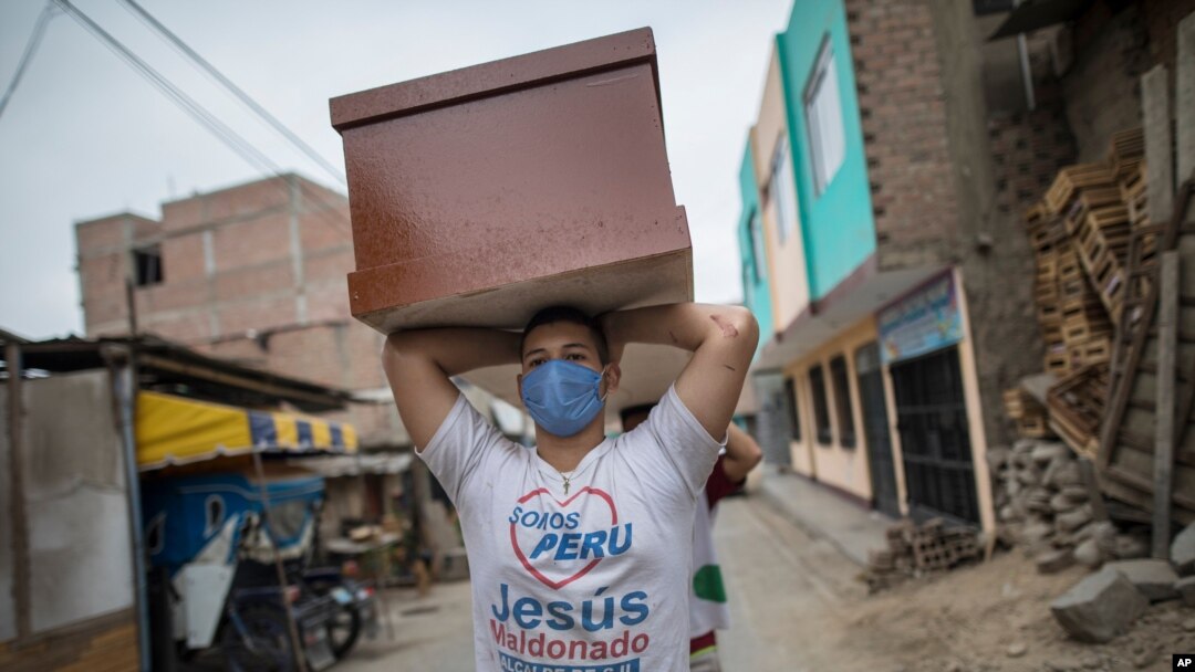 FILE - A worker, a migrant from Venezuela, carries a newly made coffin for victims of COVID-19 to a storeroom at a coffin factory in Lima, Peru, June 4, 2020. 