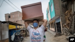 FILE - A worker, a migrant from Venezuela, carries a newly made coffin for victims of COVID-19 to a storeroom at a coffin factory in Lima, Peru, June 4, 2020. 