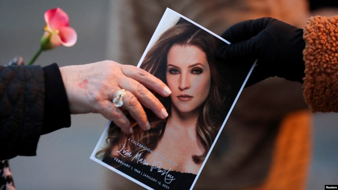 FILE: Seorang penggemar musik menyerahkan foto Lisa Marie Presley kepada penggemar lain saat menghadiri peringatan publik untuknya, satu-satunya putri "Raja Rock 'n' Roll," Elvis Presley, di Graceland Mansion di Memphis, Tennessee, AS 22 Januari 2023. 9REUTERS/Nikki Boertman)
