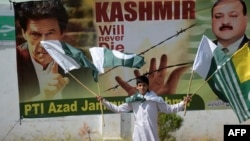 A Pakistani Kashmiri youth holds Pakistani and Kashmiri flags as he walks past a banner featuring a photograph of Pakistan's Prime Minister Imran Khan, left, during a rally in Muzaffarabad, Sept. 13, 2019. 