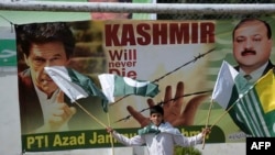 FILE - A Pakistani Kashmiri youth holds Pakistani and Kashmiri flags as he walks past a banner featuring a photograph of Pakistan's Prime Minister Imran Khan, left, during a rally in Muzaffarabad, Sept. 13, 2019. 