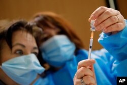 FILE - Nurses prepare a Pfizer-BioNTech COVID-19 vaccine to be administered to a health care worker at a coronavirus vaccine center in Poissy, France, January 8, 2021.