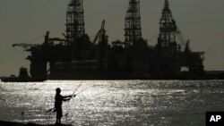 FILE - A man wears a face mark as he fishes near docked oil drilling platforms, on May 8, 2020, in Port Aransas, Texas. 