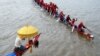 A Cambodian man, left, prays as participants row their dragon boat during a rehearsal for the Cambodian Water Festival on the Tonle Sap river in Phnom Penh on Nov. 26, 2023.