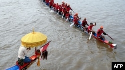 A Cambodian man, left, prays as participants row their dragon boat during a rehearsal for the Cambodian Water Festival on the Tonle Sap river in Phnom Penh on Nov. 26, 2023.