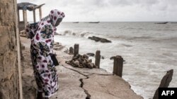 FILE - A woman looks at a crack in the walkway that leads to the mosque in Bargny, Senegal, on September 18, 2020. Fishing villages like Bargny have been fighting the rising seas for decades.
