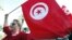 FILE - A woman waves a Tunisia flag during a rally to protest against religious and political violence in Tunis, Oct. 22, 2012. 