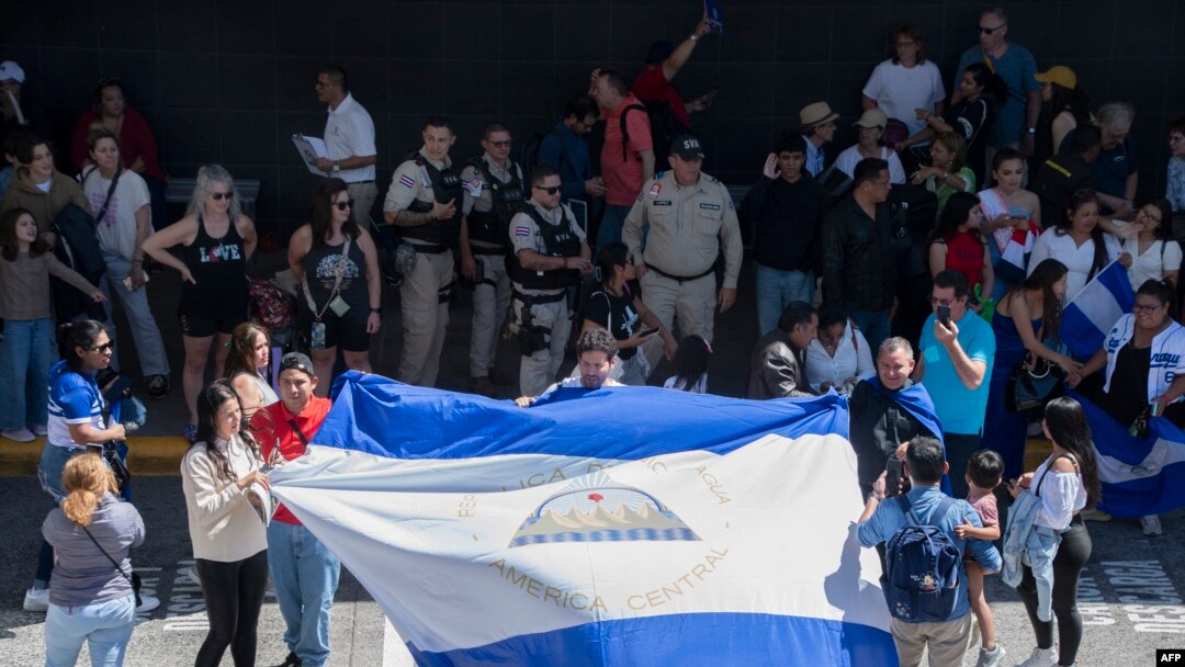 Nicaragüenses residentes en Costa Rica exhiben una bandera nicaragüense durante la llegada de la Miss Universo nicaragüense Sheynnis Palacios al Aeropuerto Internacional Juan Santa María en Alajuela, Costa Rica, el 26 de febrero de 2024. (Foto de Ezequiel BECERRA / AFP)