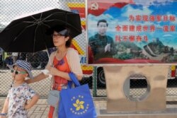 FILE - Visitors walk past a poster featuring Chinese President Xi Jinping during an open day of Stonecutter Island naval base, in Hong Kong to mark the 22nd anniversary of Hong Kong handover to China, June 30, 2019
