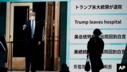 People walk past a screen in Tokyo, Japan, showing the news report that President Donald Trump has left a hospital to return to the White House after receiving treatments for COVID-19.