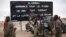 Malian soldiers are stationed at the entrance of of Gao, northern Mali, Jan. 28, 2013. The sign, a reminder of Islamic extremists, reads "Al Hesbah, together for the pleasure of God almighty and the struggle against sins."