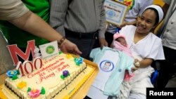 ဖိလစ်ပိုင်ရဲ့ သန်းတစ်ရာမြောက် လူဦးရေဖြစ်တဲ့ Chonalyn ကို မိခင်ဖြစ်သူ Dailin Duras Cabigayan က ပွေ့ချီထားပြီး အစိုးရပေးတဲ့ မွေးနေ့ကိတ်ကို လက်ခံနေစဉ်။ (ဂျူလိုင် ၂၇၊ ၂၀၁၄)