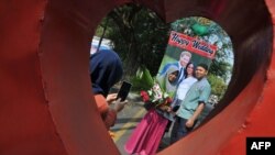 Sepasang kekasih di Solo, berfoto di depan poster Pangeran Harry dan istrinya, Meghan Markle, 20 Mei 2018. (Foto: AFP)