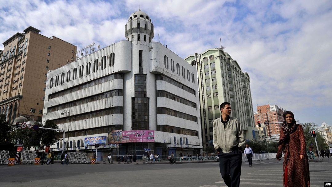 FILE - A man and a woman walk past the Rebiya Kadeer Trade Center, center, on Sept. 6, 2009, in Urumqi, in China's western Xinjiang region. The building, once once a vibrant hub for more than 800 mostly Uyghur-owned businesses, was recently demolished.