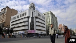 FILE - A man and a woman walk past the Rebiya Kadeer Trade Center, center, on Sept. 6, 2009, in Urumqi, in China's western Xinjiang region. The building, once once a vibrant hub for more than 800 mostly Uyghur-owned businesses, was recently demolished.