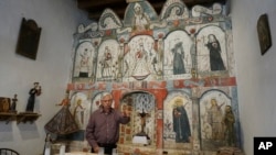 Master santero Felix Lopez speaks during an interview while standing in front of the 1810s 'reredo' or altarpiece he cleaned and preserved in the Holy Rosary Mission Church in Truchas, New Mexico, April 16, 2023. 