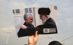 FILE - A man holds a picture of Iran's Supreme Leader Ayatollah Ali Khamenei (R) with Quds Force top commander Qassem Soleimani, during a demonstration in Tehran, Iran, Jan. 3, 2020.
