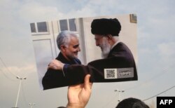 A man holds a picture of Iran's supreme leader Ali Khamenei with Iranian Revolutionary Guards top commander Qasem Soleimani (L) during a demonstration in Tehran, Jan. 3, 2020 against the killing of the top commander in a US strike in Baghdad.